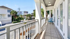A balcony with a white railing, a blue chair, and a view of neighboring houses and palm trees.