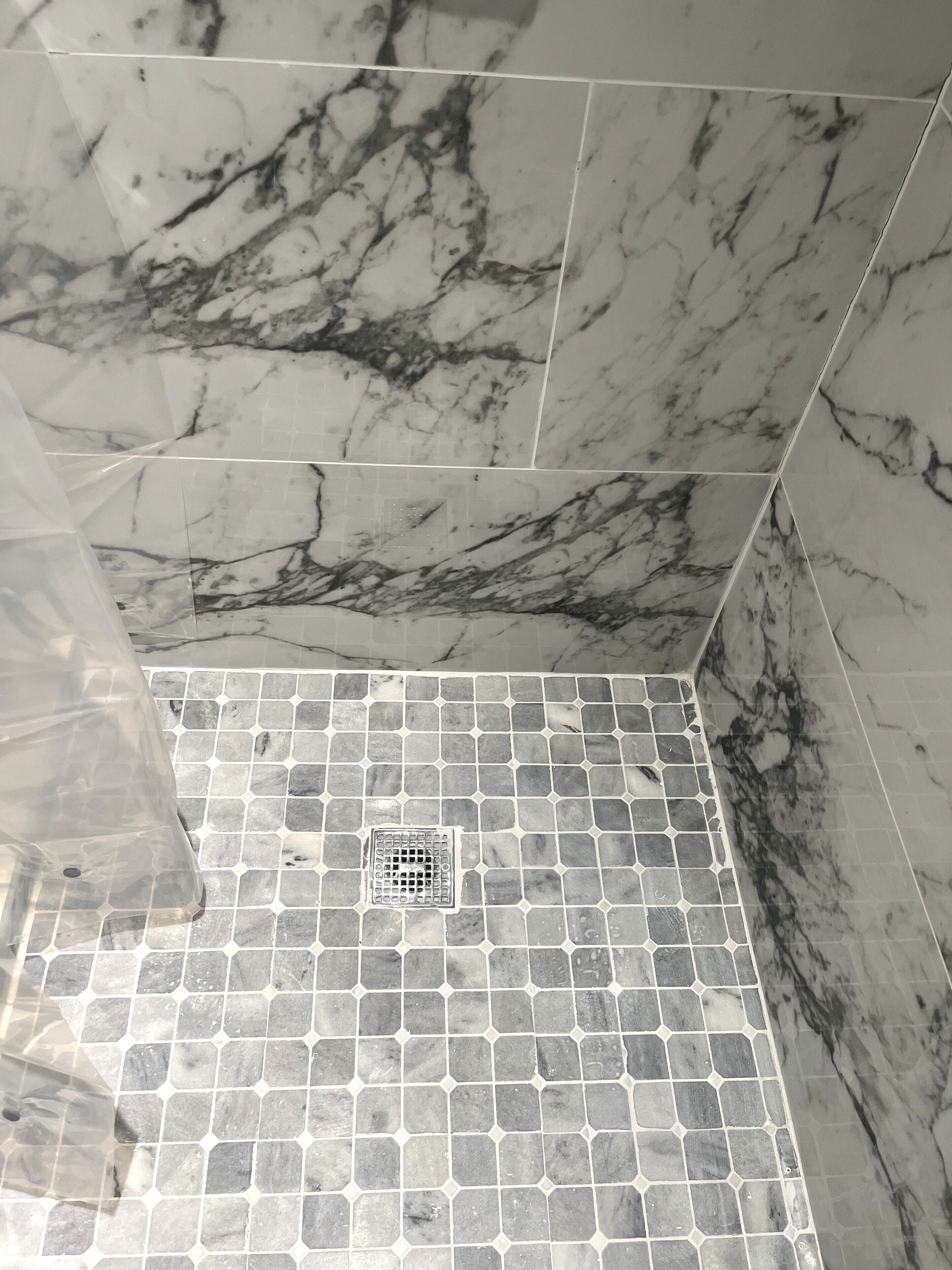 A tiled shower area with a drain in the center, surrounded by square tiles and a marble wall.