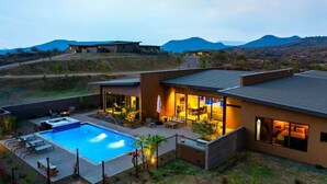 Ein modernes Haus mit Swimmingpool, Sitzgelegenheiten im Freien und Blick auf Berge.