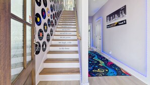 A staircase with vinyl records on the wall, a colorful carpet, and a cityscape sign. - Friends in Skyline Places, 10 min to Broadway, Perfect for Groups! (Nashville)