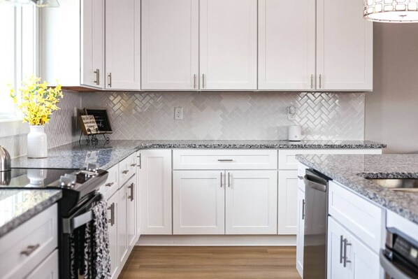 A modern kitchen with white cabinets, granite countertops, and a herringbone tile backsplash.