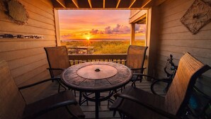 Eine Holzterrasse mit einem runden Tisch und vier Stühlen, mit Blick auf einen Sonnenuntergang.