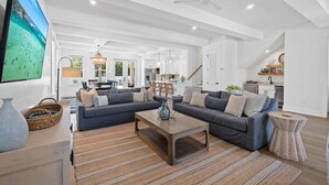 Ein großzügiges Wohnzimmer mit einem großen Flachbildfernseher, einem grauen Ecksofa, einem Holztisch und einem Streifenmuster-Teppich.