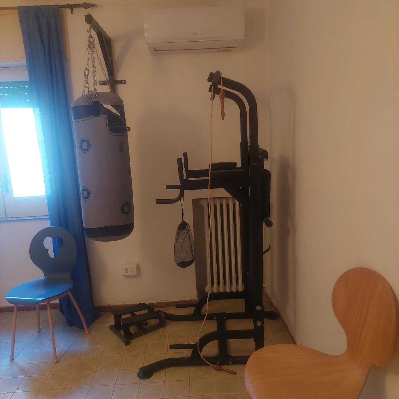 Ein Zimmer mit einem Boxsack, einem Stuhl, einem Heizkörper und einem Fenster mit Vorhängen.