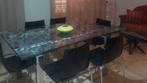 Un área de comedor con una mesa de vidrio, sillas negras, un objeto amarillo sobre la mesa y un sofá rojo al fondo.