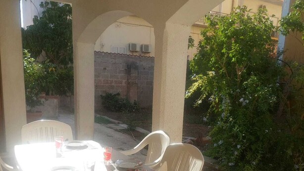 Un espacio exterior cubierto con comedor, una mesa preparada para dos personas, rodeada de sillas blancas.