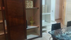 Una habitación con un aparador de madera, una mesa de vidrio y un estante blanco.