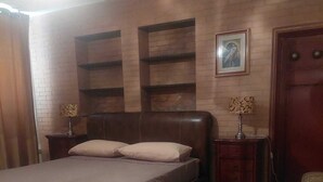 Un dormitorio con una cama grande, cabecera de madera, dos mesitas de noche con lámparas, un armario de madera y un retrato enmarcado en la pared.