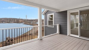 A covered deck with a view of a lake, a sliding glass door, and a white railing.