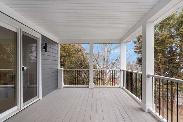 A covered porch with a white railing, a sliding glass door, and a view of trees and sky.
