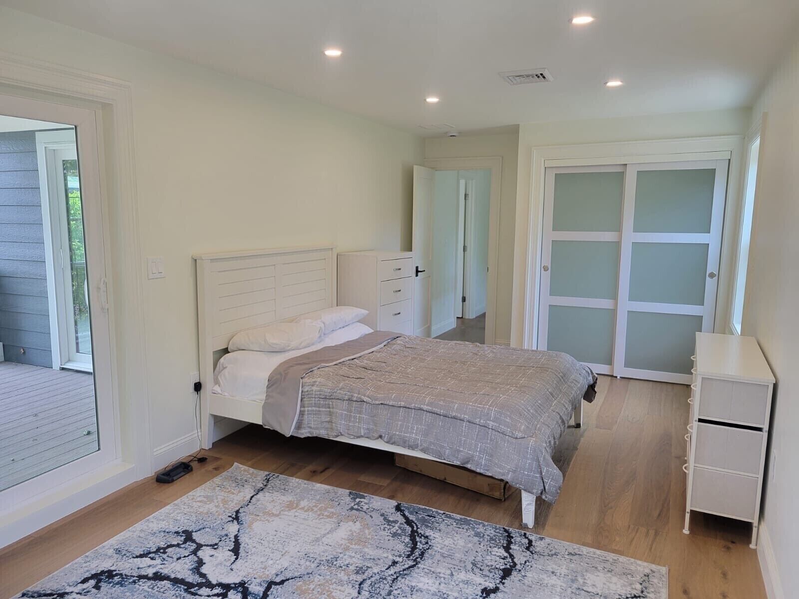 Un dormitorio con cama, mesita de noche, cómoda y puerta corrediza que da a un balcón.