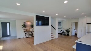 A spacious living area with hardwood flooring, a kitchen with white cabinetry, a dining area, and a staircase leading to another level.