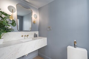 A bathroom with a marble sink, gold fixtures, a large mirror, and a potted plant. - Luxury Waterfront House in Portsmouth, RI with Direct Beach Access (Portsmouth)