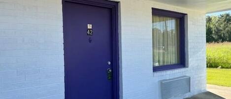 A building with a dark blue door marked with the number 42, a window with a curtain, and a small vent on the wall.