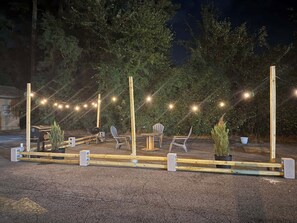 Un espace extérieur aménagé avec des guirlandes lumineuses, des chaises, une table et un barbecue.