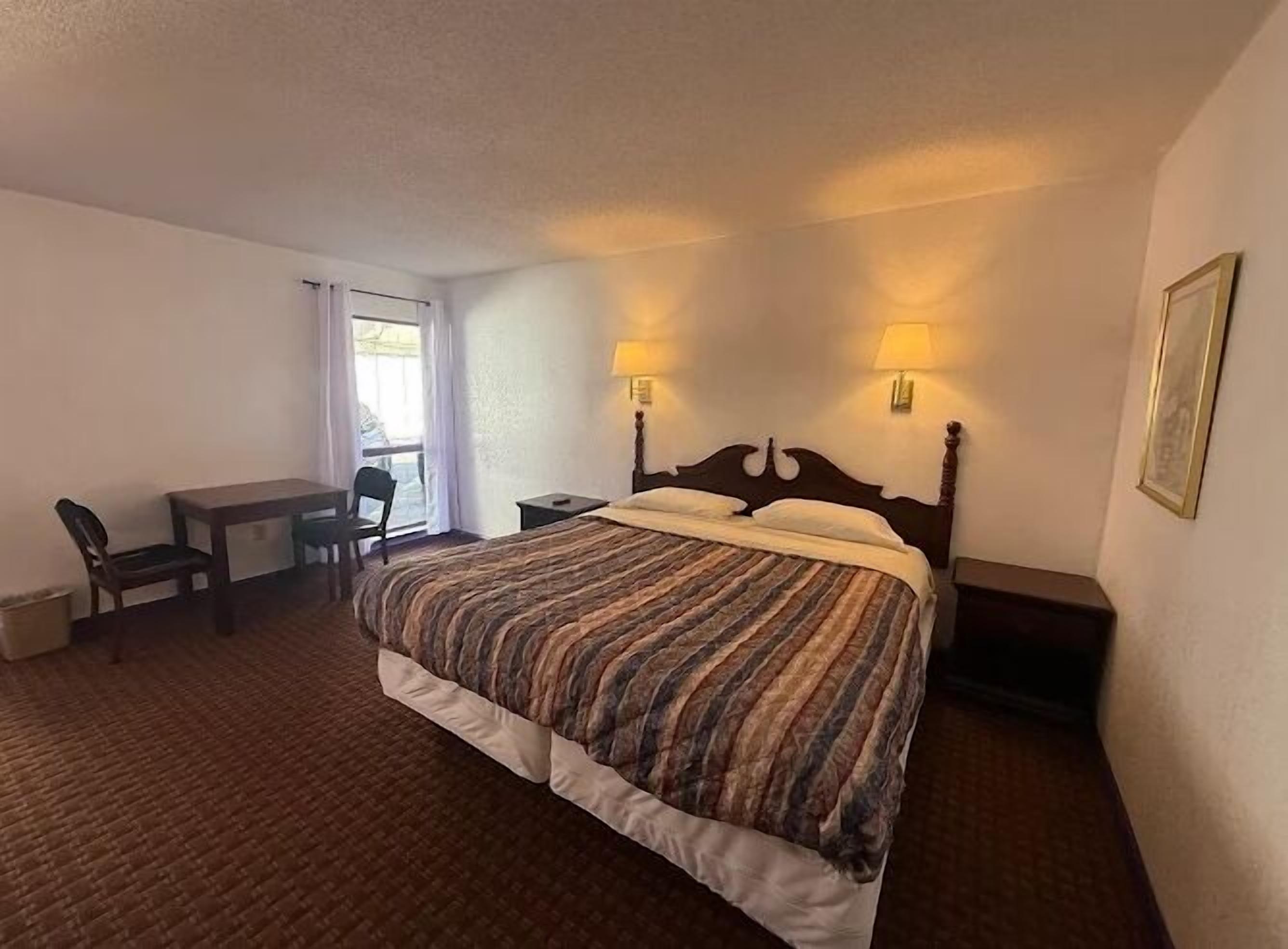 Une chambre d’hôtel avec un lit simple, un bureau, deux chaises et une fenêtre avec des rideaux.