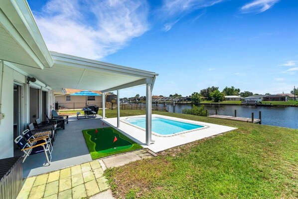 A covered patio with outdoor seating, a pool, and a small putting green.