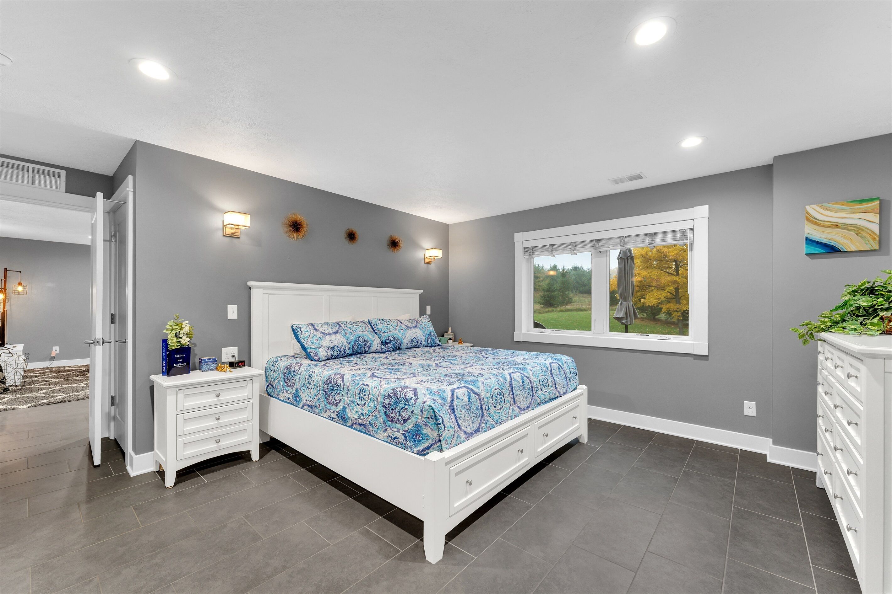 A bedroom with a bed, nightstands, a dresser, and a window with a view of trees.