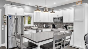 Una cocina moderna con gabinetes blancos, electrodomésticos de acero inoxidable y una isla central con asientos.