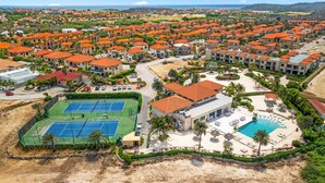 Ein Luftbild eines Resorts mit mehreren Gebäuden, einem Tennisplatz und einem Schwimmbad.