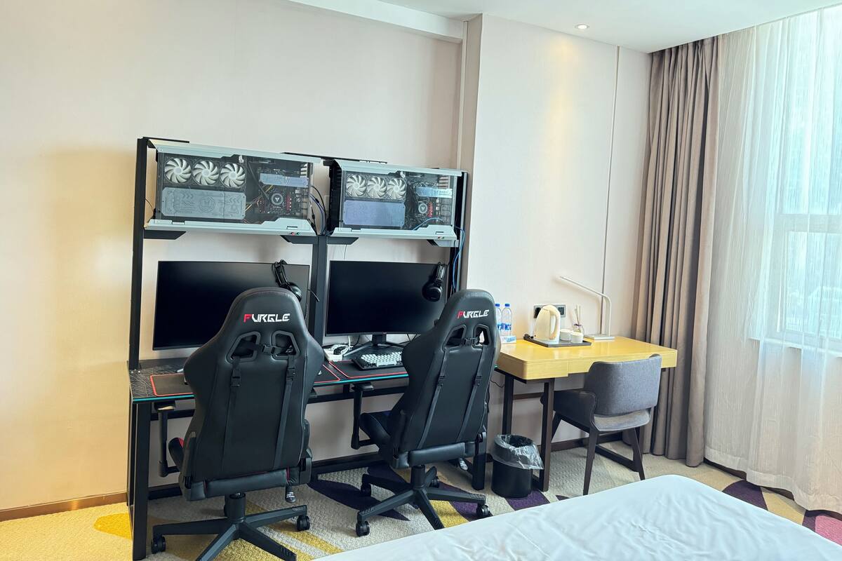A hotel room with a desk, two gaming chairs, a large monitor, and a second monitor.