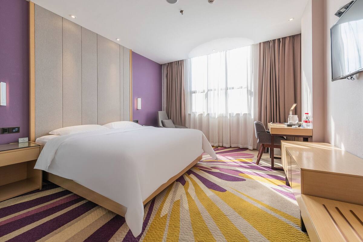 A hotel room with a large bed, a desk, a chair, and a TV.