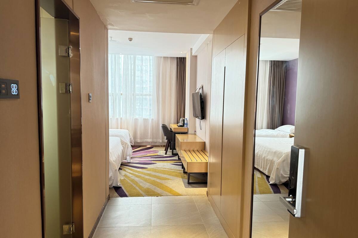 A hotel room with two beds, a desk, a chair, a TV, and a bathroom with a mirror.