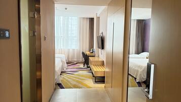 A hotel room with two beds, a desk, a chair, a TV, and a bathroom with a mirror.