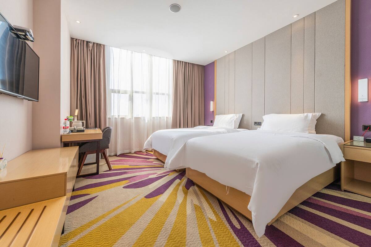 A hotel room with two beds, a desk, a chair, and a TV.
