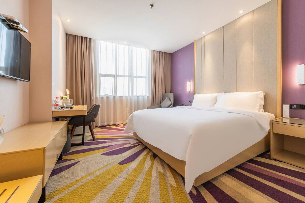 A hotel room with a large bed, a desk, a chair, and a TV.