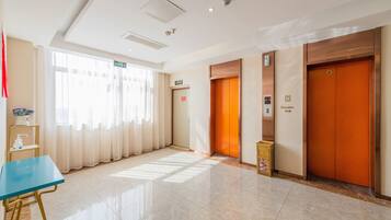 Un vestíbulo de hotel con una mesa azul, dos ascensores y una vista despejada del exterior a través de amplias ventanas.