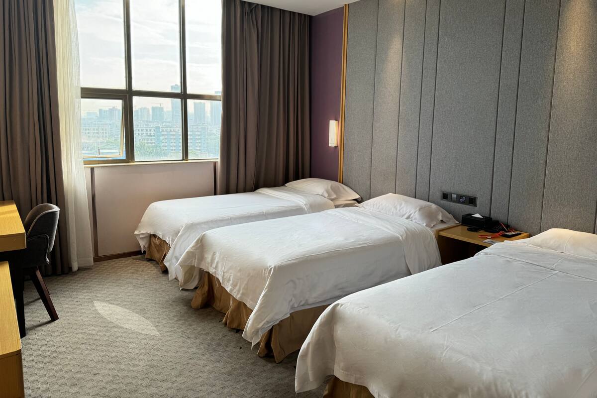 A hotel room with two beds, a desk, and a view of the city.