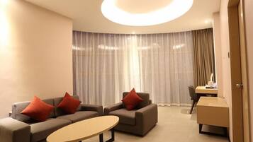 A modern hotel room with a sofa set, a small table, and a desk with a chair.