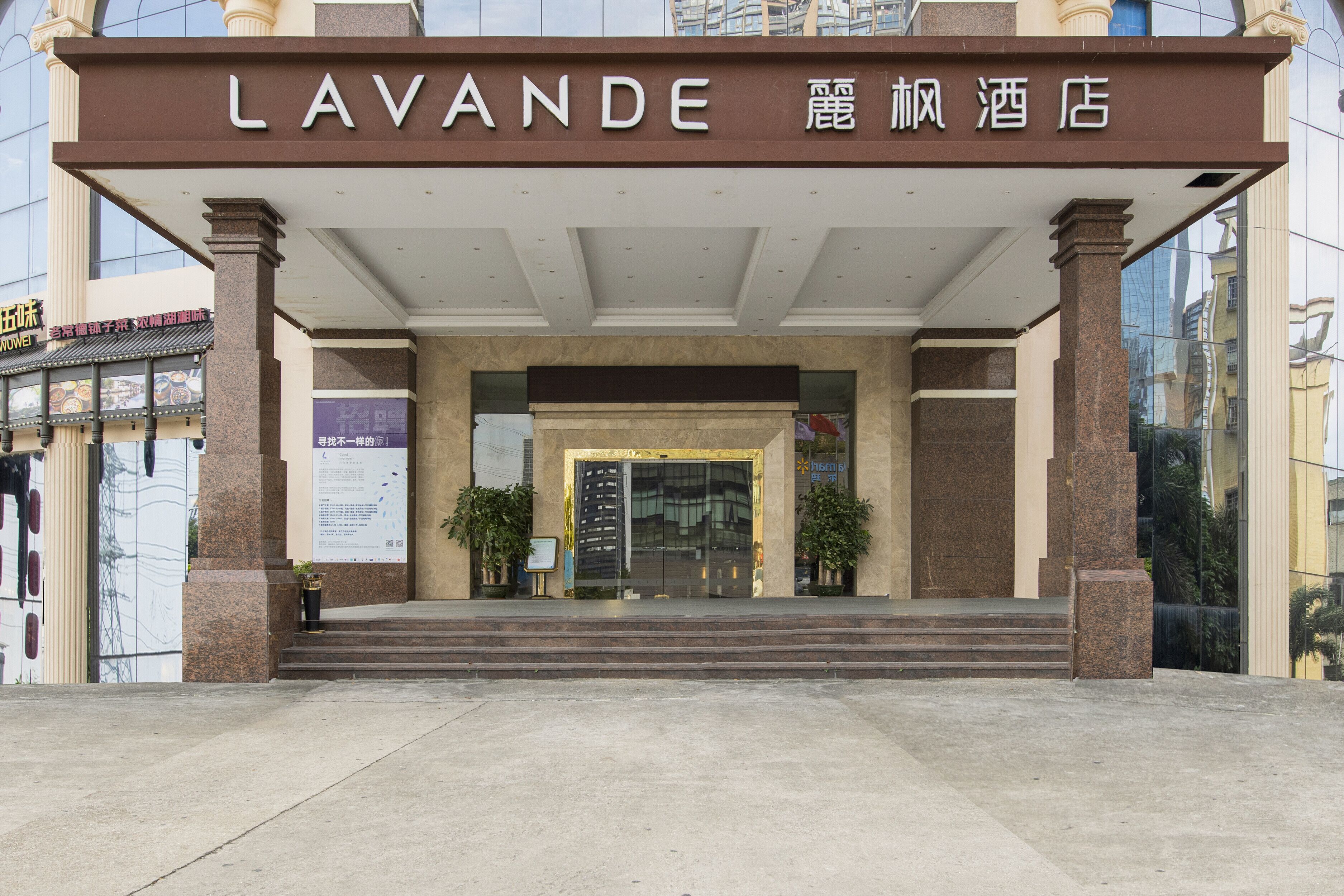 The entrance to the Lavender hotel with a prominent sign, a set of steps leading up to the entrance, and a glass facade reflecting the surroundings.