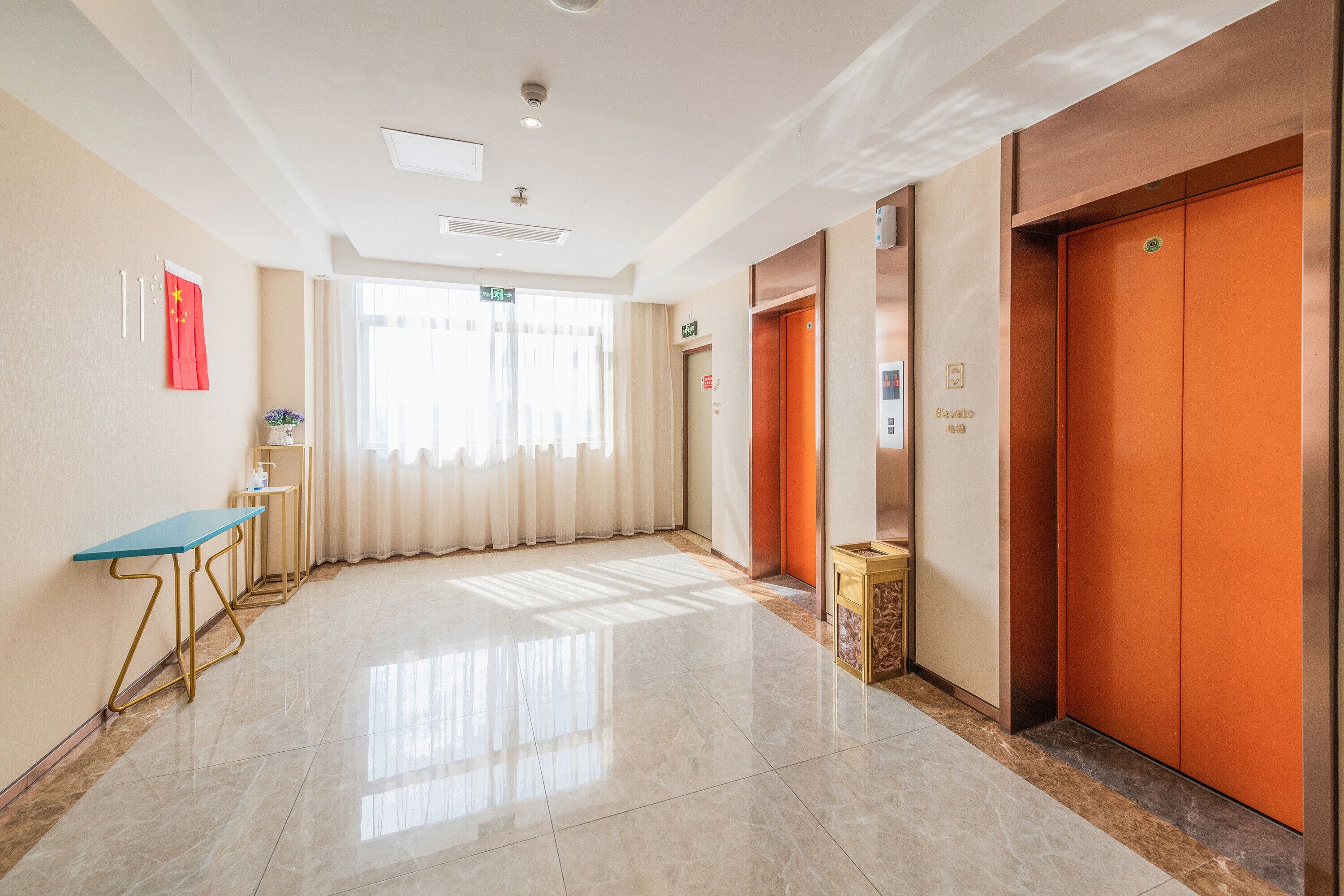 A hotel corridor with a blue table, a red flag, and an elevator.