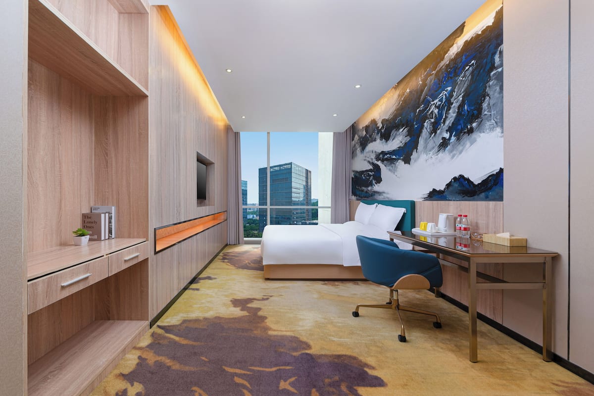 A modern hotel room with a bed, desk, and a large window offering a city view.