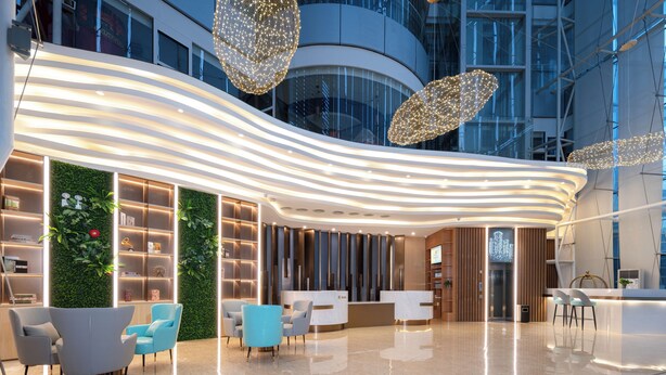 Un lobby moderno de hotel con un mostrador de recepción curvo, zona de estar y una pared verde con plantas.