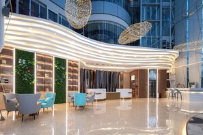 A modern hotel lobby with a curved reception desk, seating area, and a green wall with plants. - Trendy Romantic Hotel International Guangzhou Baoneng Performing Arts Center Science City Metro Station Branch (Guangzhou)