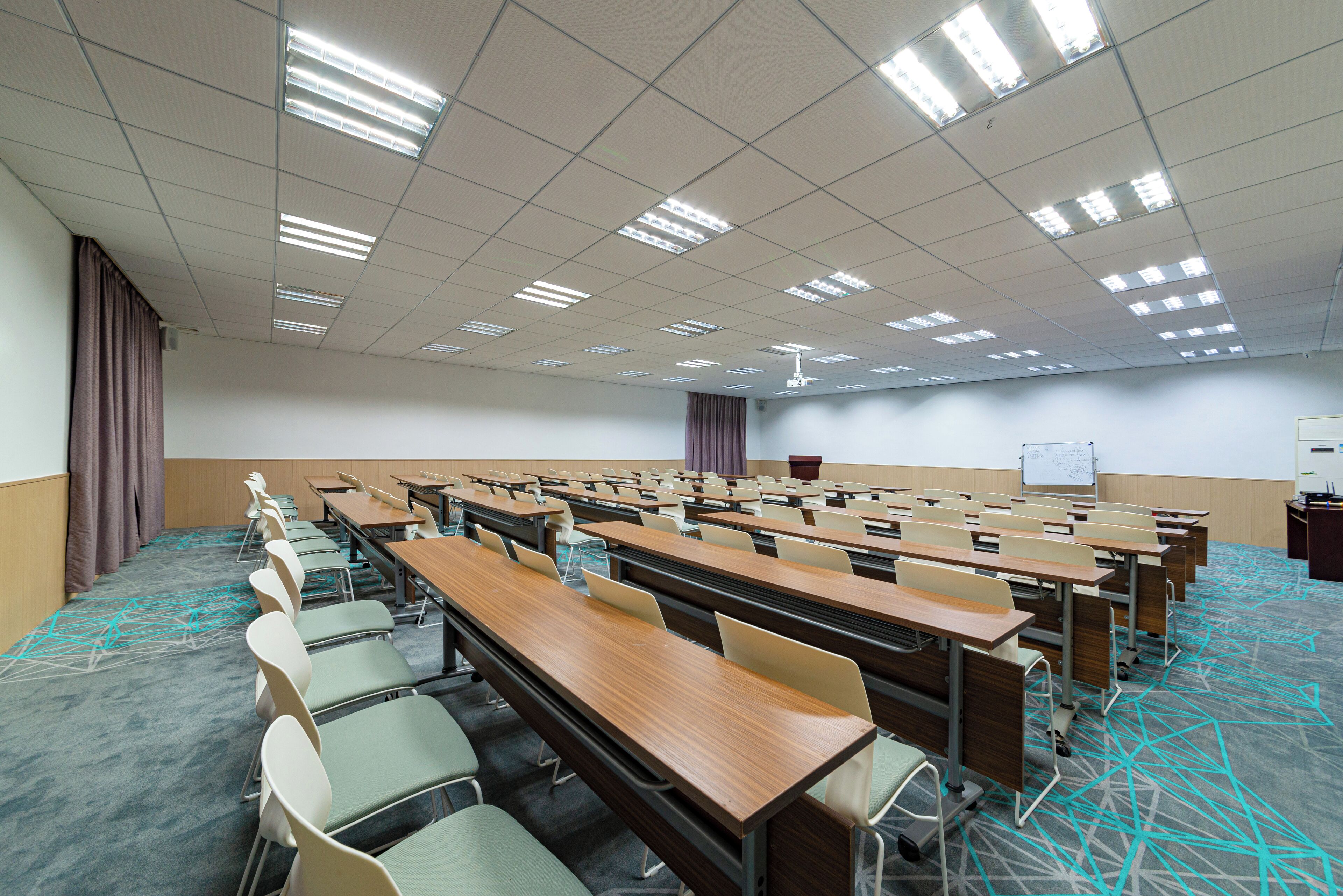 A conference room with rows of tables and chairs, a whiteboard, and a projector screen.