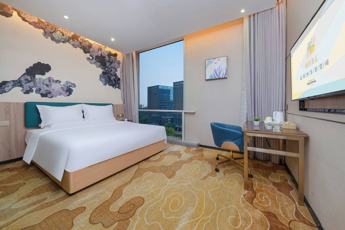 A hotel room with a large bed, a desk, a chair, and a view of the cityscape.