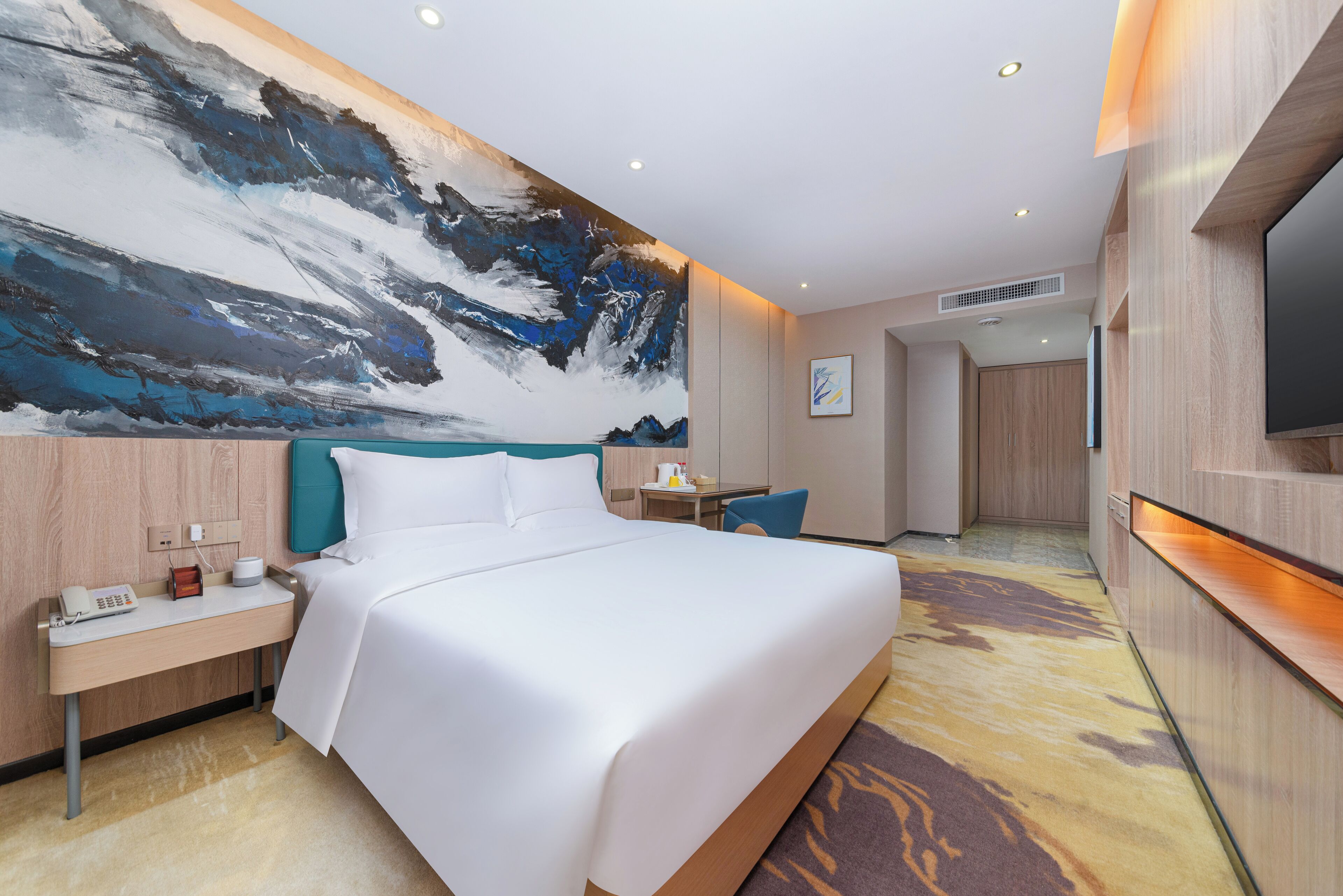 Een moderne hotelkamer met een groot bed, een bureau, een telefoon en een schilderij aan de muur.