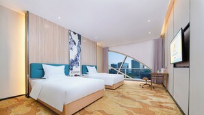 Una habitación de hotel con dos camas, un escritorio, televisión y vistas a la ciudad.