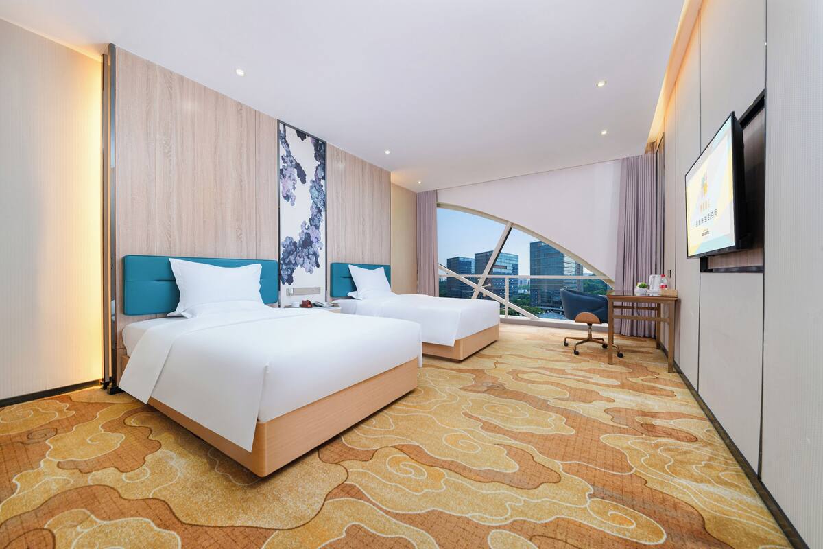 A hotel room with two beds, a desk, a TV, and a city view.