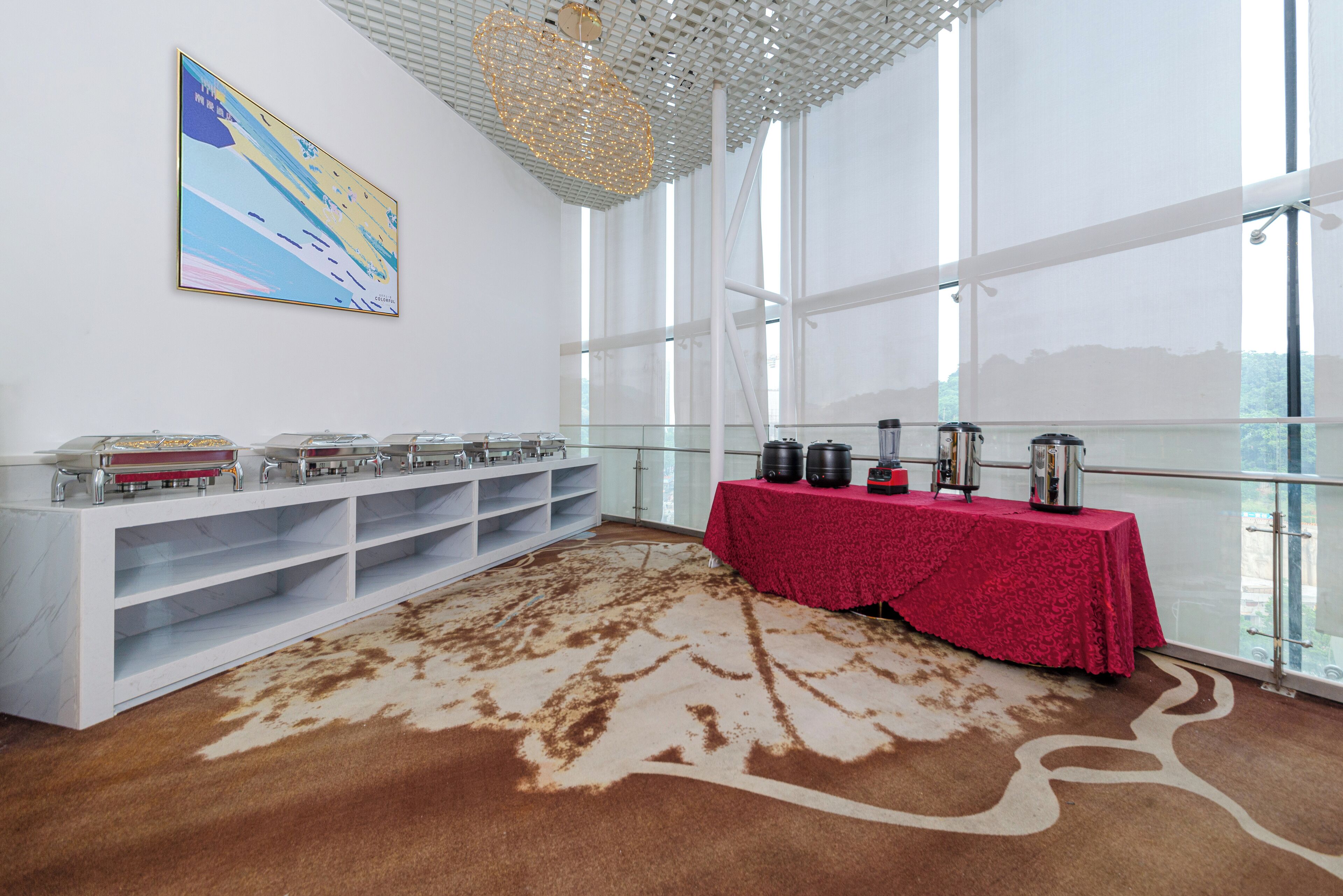 A room with a large window, a table with a red tablecloth, and a white console with shelves.