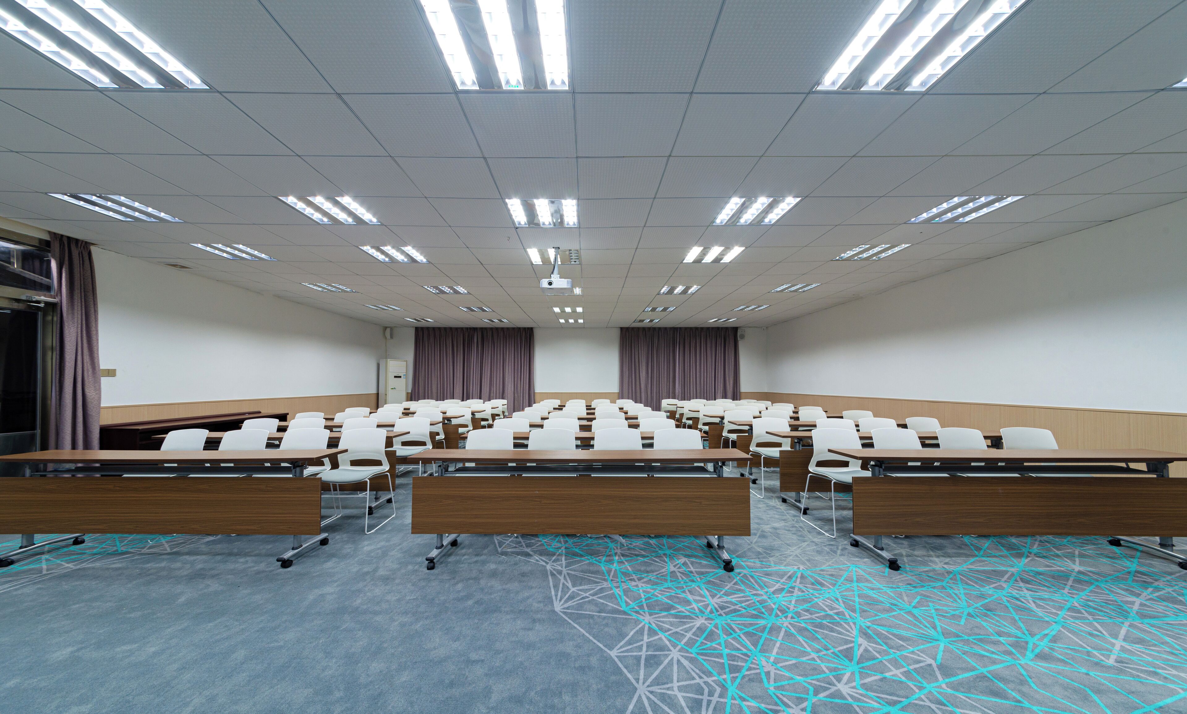 A conference room with rows of desks and chairs, a projector, and a large screen.