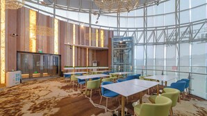 Un espacio interior moderno con mesas y sillas, un muro de cristal y un revestimiento de madera con luminarias verticales.