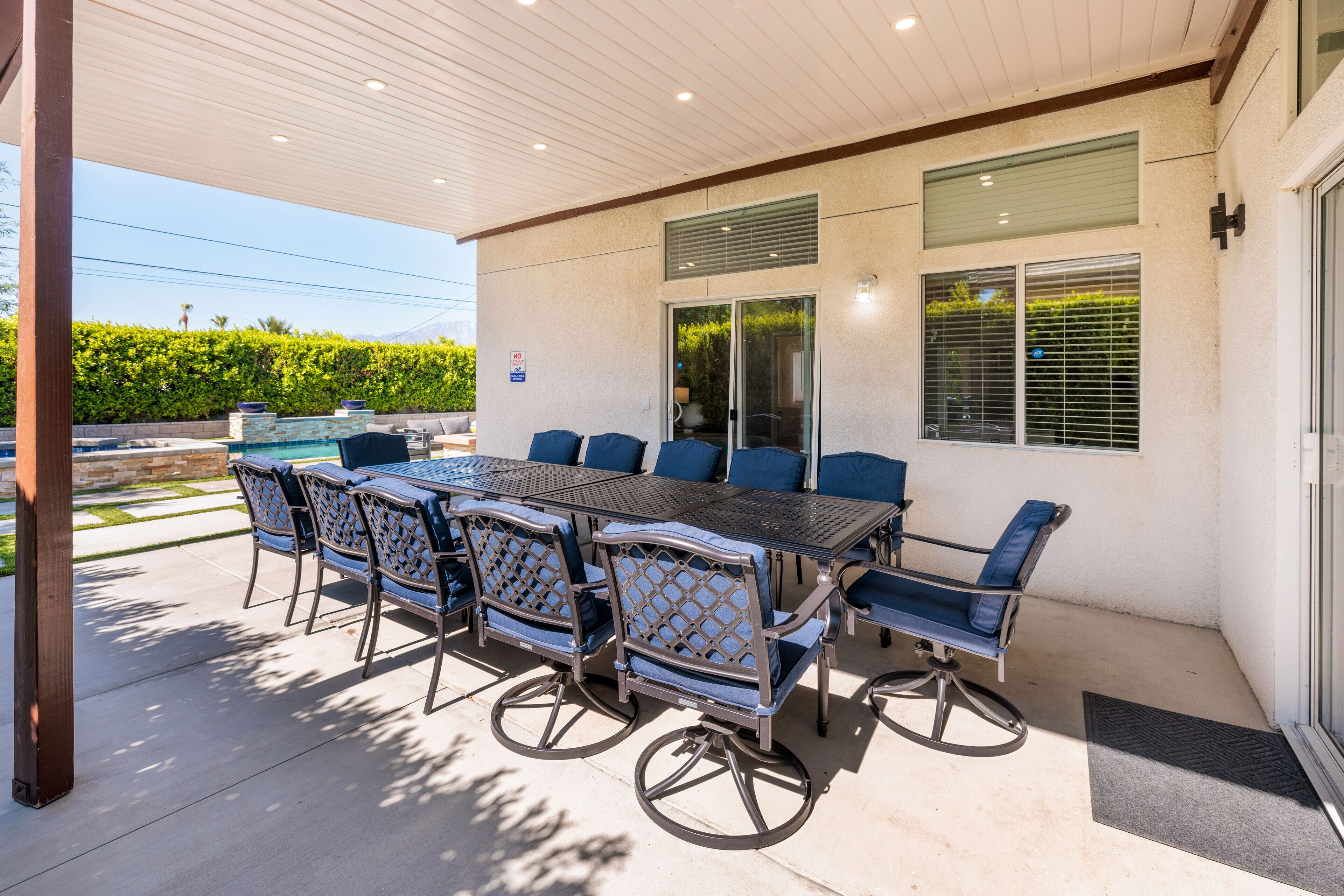 Un patio al aire libre con una mesa rectangular y seis sillas, techo cubierto y vista a la montaña.