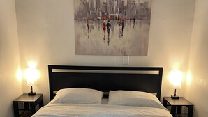 A neatly made bed with a patterned bedspread, two bedside lamps, and a cityscape painting on the wall. - Entire house close to downtown Sandusky on a quiet street (Sandusky)