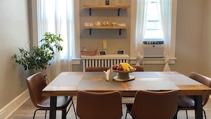 A dining area with a wooden table, four brown chairs, a plant, and shelves with wine glasses and bottles. - Entire house close to downtown Sandusky on a quiet street (Sandusky)