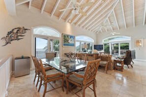 A spacious dining area with a glass table and wooden chairs, a ceiling fan, and a view of the outdoors. - Oceanfront | Peterborg | Infinity Pool | Generator (Sydneys Fancy)